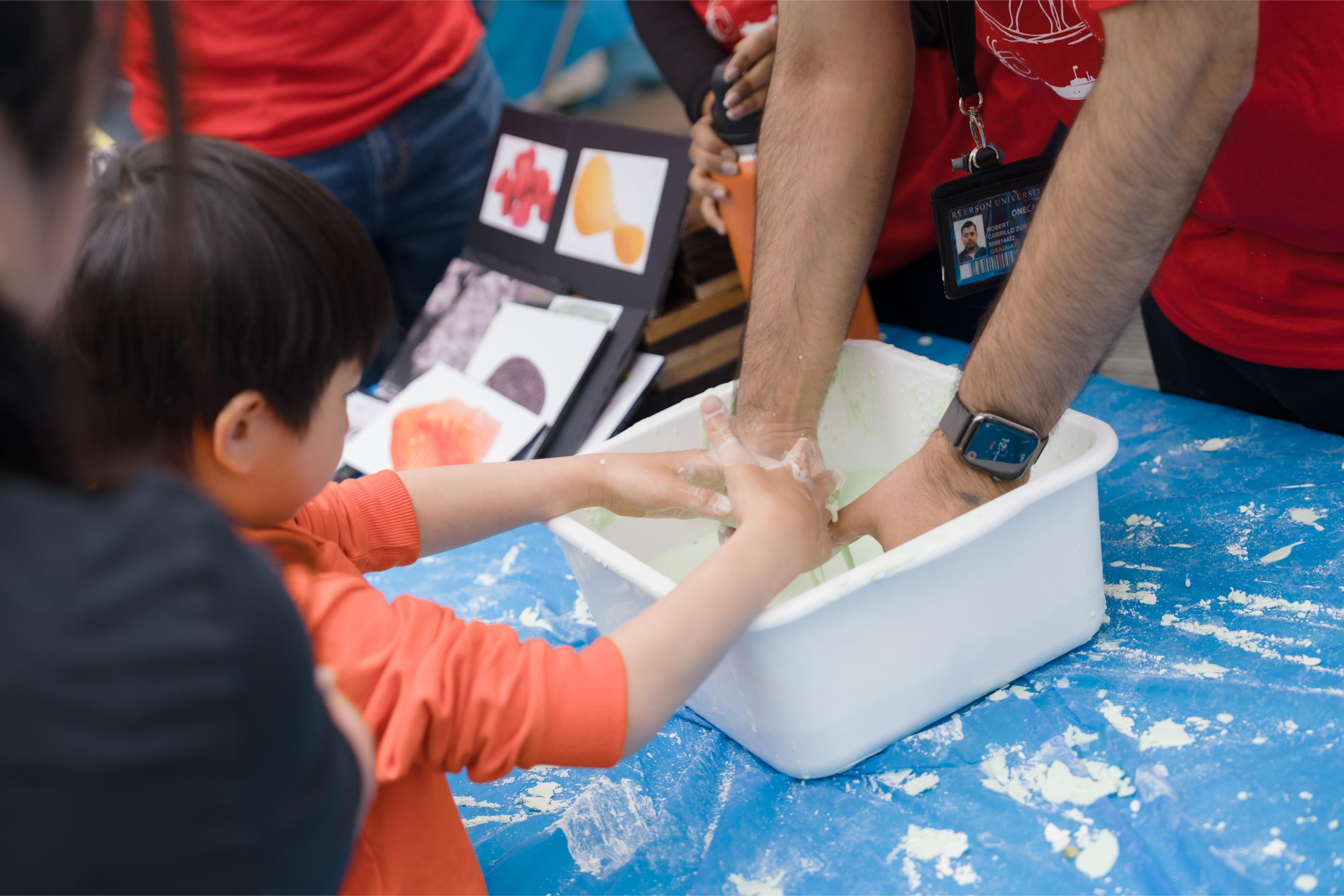 A child making green slime with a volunteer in a white container at the Food Science Now booth.